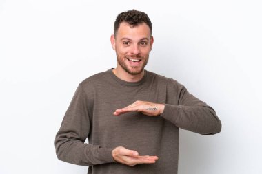 Beyaz arka planda izole edilmiş genç Brezilyalı bir adam bir ilan vermek için avucunun içinde hayali bir mekan tutuyor.