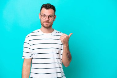 Mavi arka planda izole edilmiş genç Brezilyalı bir adam bir ürün sunmak için kenarı işaret ediyor