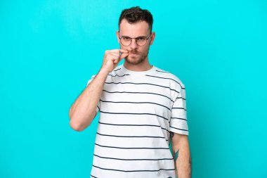 Mavi arka planda izole edilmiş genç Brezilyalı bir adam sessizlik işareti gösteriyor.