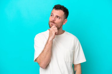 Genç Brezilyalı adam mavi arka planda izole edilmiş ve yukarı bakıyor.