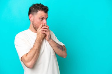 Genç Brezilyalı adam mavi arka planda izole edilmiş ağzını kapatıyor ve yana bakıyor.