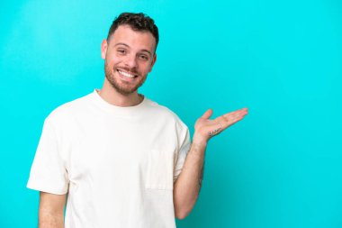 Mavi arka planda izole edilmiş genç Brezilyalı bir adam bir ilan vermek için avucunun içinde hayali bir alan tutuyor.