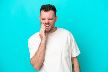 Mavi arka planda diş ağrısı olan genç Brezilyalı bir adam izole edilmiş.