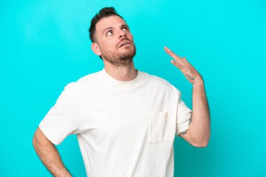 Genç Brezilyalı adam mavi arka planda izole edilmiş, yorgun ve hasta bir ifadeyle.