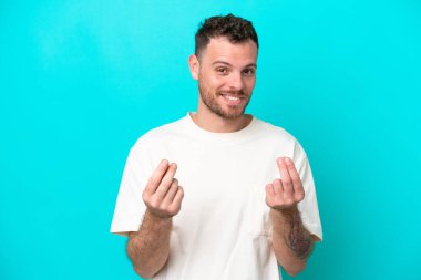 Mavi arka planda izole genç Brezilyalı adam para hareketi yapıyor.