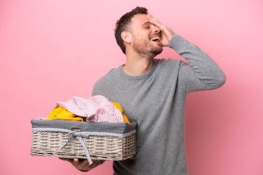 Genç Brezilyalı bir adam pembe arka planda izole edilmiş bir çamaşır sepeti tutuyor. Çok gülümsüyor.
