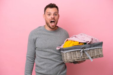 Genç Brezilyalı bir adam pembe bir arka planda yüz ifadesi ile izole edilmiş bir kıyafet sepeti tutuyor.