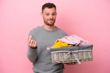 Genç Brezilyalı bir adam pembe arka planda izole edilmiş bir çamaşır sepeti tutuyor ve para hareketi yapıyor.