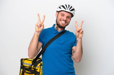 Beyaz arka planda izole edilmiş termal sırt çantalı genç Brezilyalı adam iki eliyle zafer işareti gösteriyor.