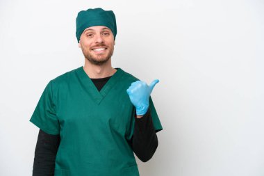 Yeşil üniformalı, beyaz arka planda izole edilmiş Brezilyalı cerrah bir ürün sunmak için kenarı işaret ediyor.