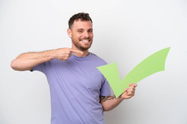 Beyaz arka planda izole edilmiş genç Brezilyalı bir adam elinde bir çek simgesi tutuyor ve onu işaret ediyor.