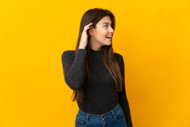 Genç Brezilyalı kız sarı arka planda izole edilmiş bir şekilde elini kulağına koyarak bir şeyler dinliyor.