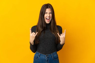 Genç Brezilyalı kız sarı arka planda izole edilmiş boynuz hareketi yapıyor.