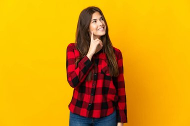 Genç Brezilyalı kız, sarı arka planda izole edilmiş bir şekilde yukarı bakarken bir fikir düşünüyor.