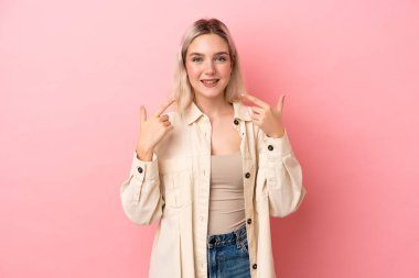 Pembe arka planda izole edilmiş beyaz bir kadın baş parmak hareketi yapıyor.