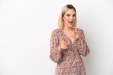 Beyaz arka planda izole edilmiş genç beyaz kadın ön tarafı işaret ediyor ve gülümsüyor.