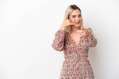 Beyaz arka planda izole edilmiş genç beyaz bir kadın telefon hareketi yapıyor ve ön tarafı işaret ediyor.