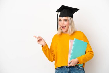 Beyaz arka planda izole edilmiş beyaz bir üniversite mezunu genç bir kadın parmak kaldırıyor ve bir ürün sunuyor.