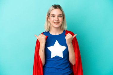 Süper Kahraman Kafkasyalı kadın mavi arka planda izole edilmiş. Baş parmakları havada ve gülümsüyor.