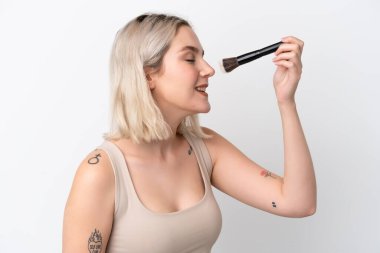 Beyaz arka planda izole edilmiş beyaz bir kadın elinde makyaj fırçası ve mutlu bir ifade var.