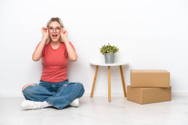 Genç bir kadın beyaz arka planda gözlüklü ve şaşırmış kutuların arasına taşınıyor.