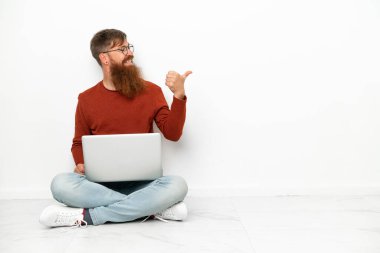 Dizüstü bilgisayarlı, beyaz arka planda izole edilmiş genç, beyaz bir adam bir ürünü sunmak için kenarı işaret ediyor.