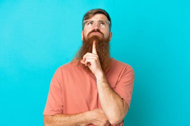 Kırmızımsı beyaz adam mavi arka planda izole edilmiş gözlüklü ve yukarı bakıyor