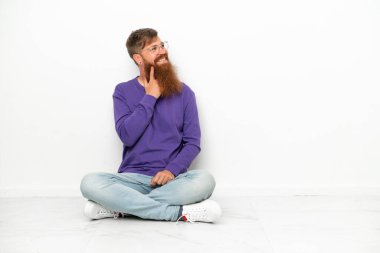 Beyaz arka planda izole bir şekilde yerde oturan Kafkasyalı genç adam yukarı bakarken bir fikir düşünüyor.