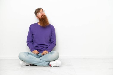 Beyaz arka planda izole bir şekilde yerde oturan Kafkasyalı genç adam...