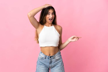 Pembe arka planda izole edilmiş beyaz bir kadın. Şaşırmış ve işaret ediyor.