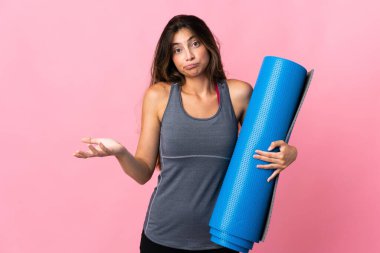 Genç sporcu kadın yoga derslerine giderken pembe arka planda izole edilmiş bir minder tutuyor. Omuzlarını kaldırırken şüpheyle hareket ediyor.