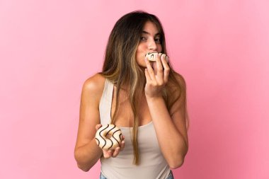 Pembe arka planda izole edilmiş beyaz bir kadın elinde donut tutuyor.