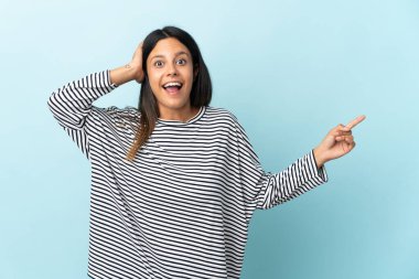 Kafkasyalı kız mavi arka planda izole edilmiş. Şaşırmış ve işaret ediyor.