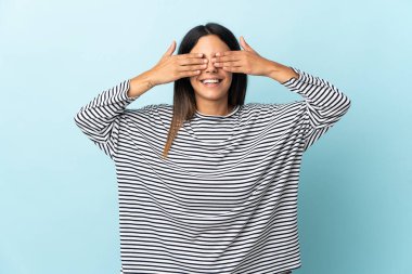 Mavi arka planda izole edilmiş beyaz bir kız. Gözleri elleriyle kaplıyor ve gülümsüyor.