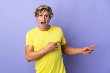Soyutlanmış mor arka plandaki İngiliz adam şaşırmış ve işaret ediyor.
