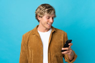 İzole edilmiş mavi arkaplan üzerindeki İngiliz adam cep telefonuyla bir mesaj ya da e-posta gönderiyor