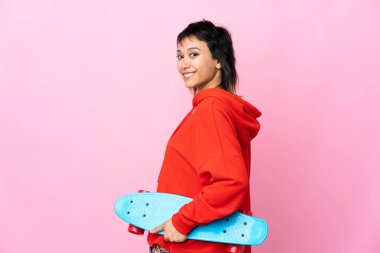 Genç Uruguaylı kadın izole pembe arka planda kaykayla geziyor.