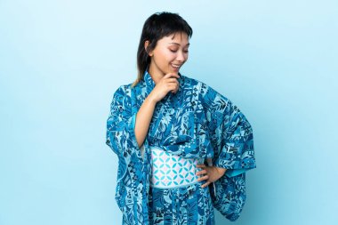 Kimono giyen genç bir kadın mavi arka planda, yana bakıyor ve gülümsüyor.