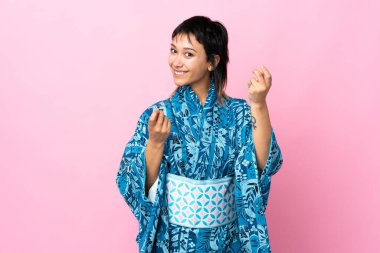 İzole edilmiş mavi arka planda kimono giyen genç bir kadın para hareketi yapıyor.
