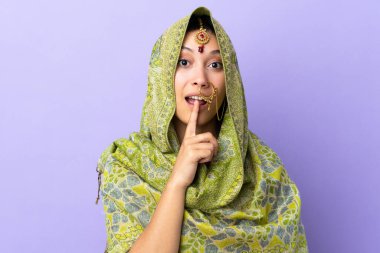 Mor arka planda izole edilmiş Hintli bir kadın sessizlik işareti gösteriyor. Parmağını ağzına koy.