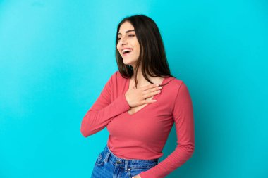 Mavi arka planda izole edilmiş genç beyaz kadın gülümserken yukarı bakıyor.