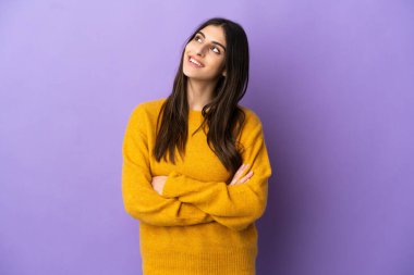 Mor arka planda izole edilmiş genç beyaz kadın gülümserken yukarı bakıyor.