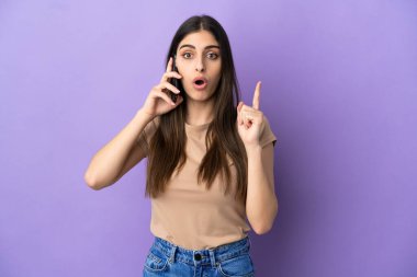 Mor arka planda izole edilmiş cep telefonu kullanan beyaz bir kadın çözümü bulmak için parmağını kaldırıyor.