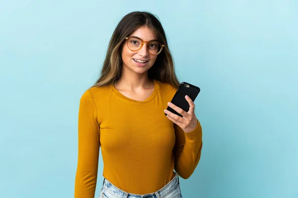 Giovane Donna Caucasica Utilizzando Telefono Cellulare Isolato Sfondo Blu Sorridente — Foto Stock