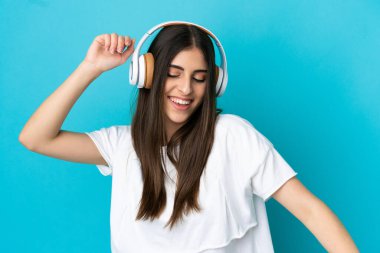 Genç beyaz kadın mavi arka planda izole edilmiş müzik ve dans dinliyor.