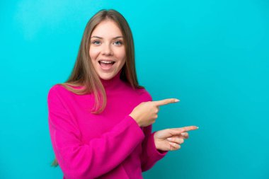 Mavi arka planda izole edilmiş genç Litvanyalı kadın şaşırmış ve işaret ediyor.