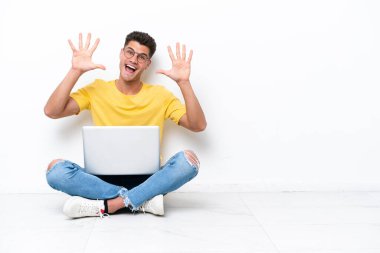 Yerde oturan genç adam beyaz arka planda izole edilmiş parmaklarıyla on kişi sayıyor.