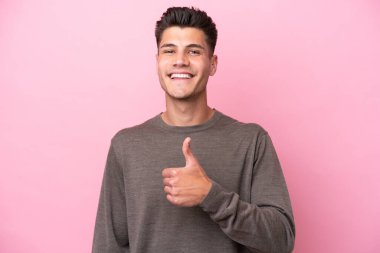 Pembe arka planda izole edilmiş genç beyaz bir adam baş parmak hareketi yapıyor.