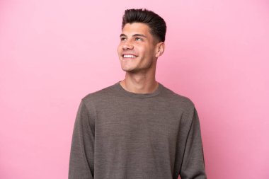 Kafkasyalı genç bir adam pembe arka planda izole edilmiş, yukarı bakarken bir fikir düşünüyor.