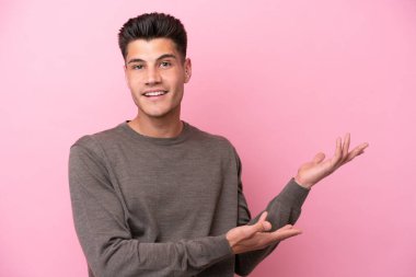 Pembe arka planda izole edilmiş genç beyaz adam, davet edilmek için ellerini yana uzatıyor.